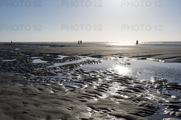 Walkers on the beach at low tide with tide pools