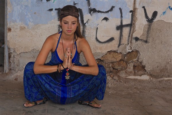 Young woman with headband doing yoga exercise with folded hands in squat position