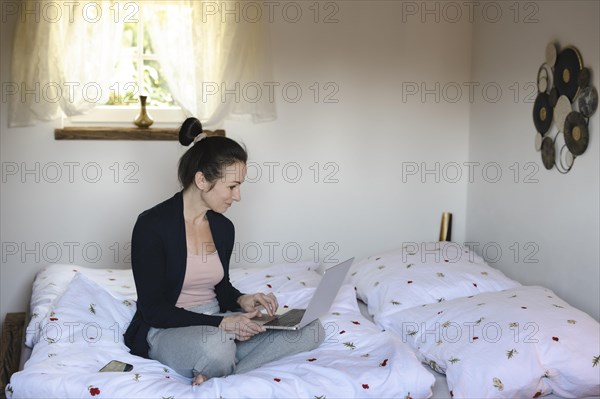 Woman sitting comfortably on bed in bedroom and working on laptop