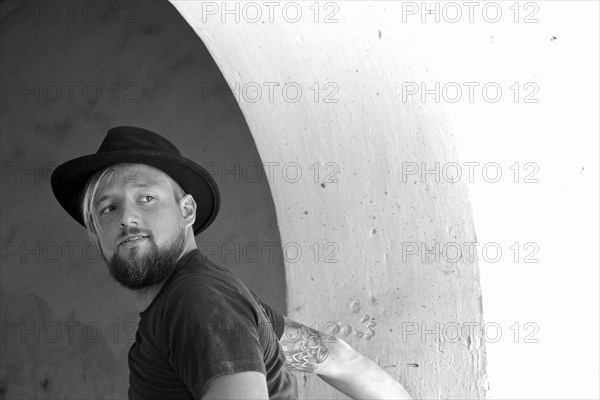 Young man with beard and black hat looks around questioningly