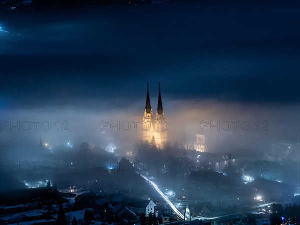 Illuminated church towers of Admont Abbey rise out of the fog
