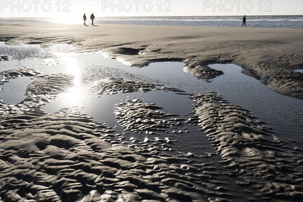 Walkers on the beach at low tide with tide pools