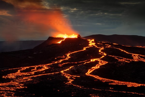 Lava spurting out of crater and reddish illuminated smoke cloud