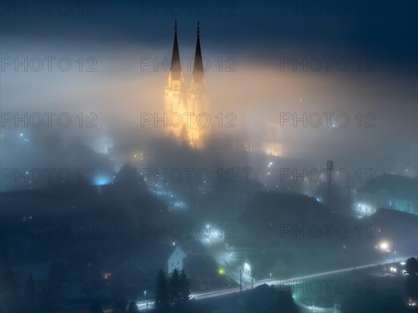 Illuminated church towers of Admont Abbey rise out of the fog