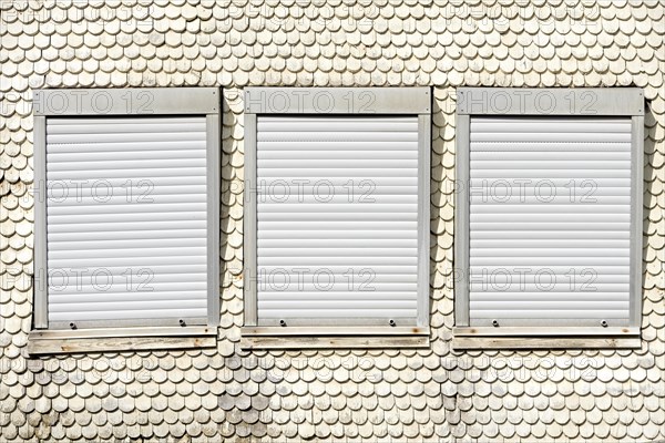 Closed plastic roller shutters in wooden historic facade made of wooden shingles