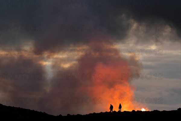 Tourists in front of reddish illuminated smoke cloud