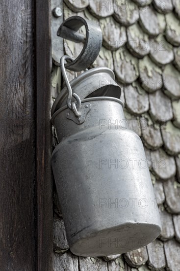 Old aluminium milk can hangs on house entrance of historic clapboard house