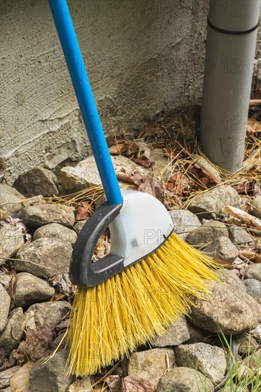 Broom in rock border leaning against exterior wall of house