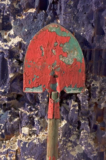 Colourful shovel with paint residue leans against purple crumbling wall