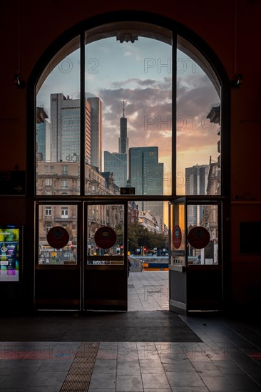 View out through the main entrance of a glass door of Frankfurt Central Station to the skyline in the romantic sunrise. A gateway to the city that is just waking up