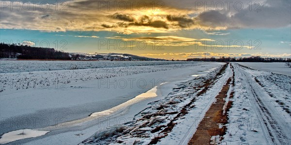 Field path with snow and sun behind clouds