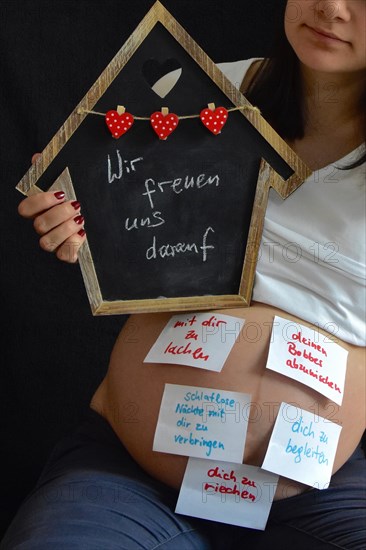 Expectant with wish list on belly holds up black board