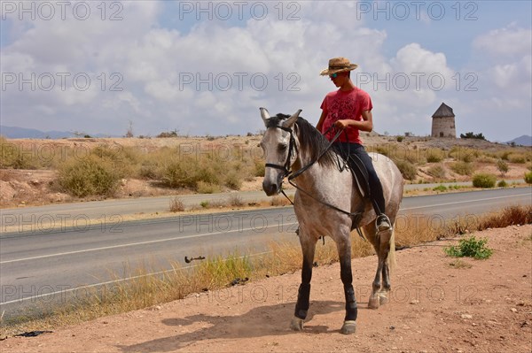 Young rider from front with straw hat in front of mill without wings