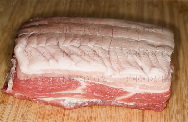 Raw lean pork belly with carved skin lies on a wooden board