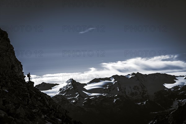 Climber on rocky outcrop with South Tyrolean mountains at blue hour