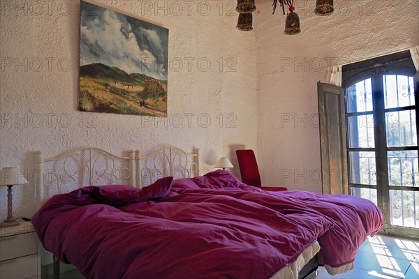 Bedroom with upholstered double bed and oil painting in front of open shutters