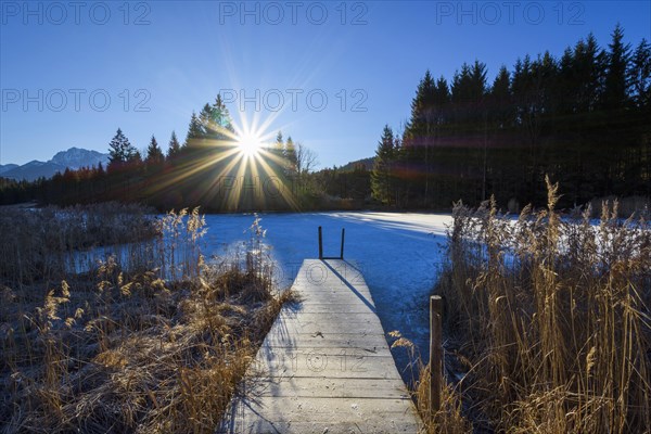 Wooden jetty with frozen lake and sun