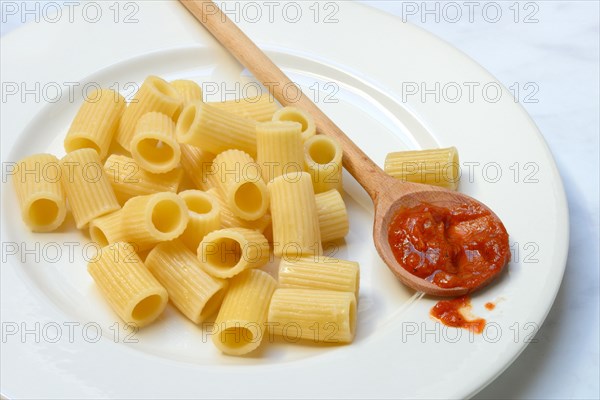 Cooked rigatoni and cooking spoon with tomato sauce