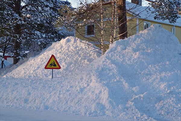 Huge snow piles and traffic sign with snowmobile in front of residential buildings