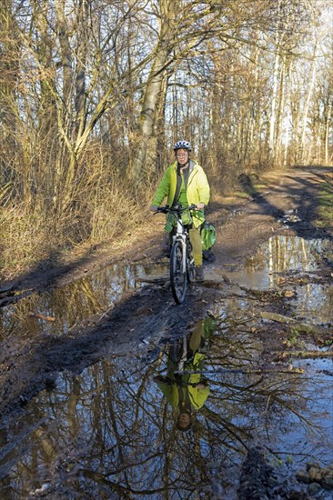 Woman cycling with e-bike over muddy forest path and through puddles