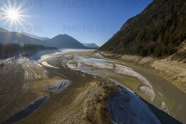 Deflated water reservoir with tourists and sun in winter