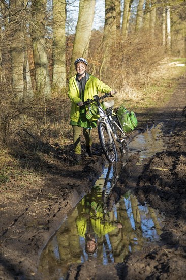 Woman cycling with e-bike over muddy forest path and through puddles