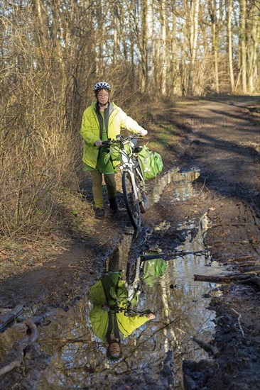 Woman cycling with e-bike over muddy forest path and through puddles