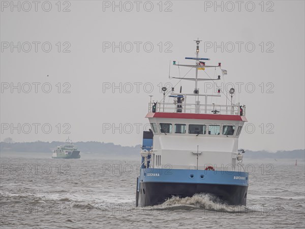 Supply ship Burchana with ferry Spiekeroog IV on the stormy North Sea entering the harbour