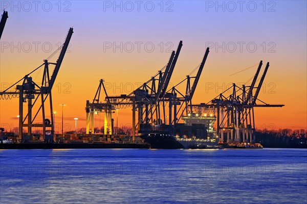 Loading cranes at the container terminal Burchardkai with a container ship at sunset