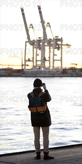 A person takes pictures of loading cranes at the Norderelbe in Altona