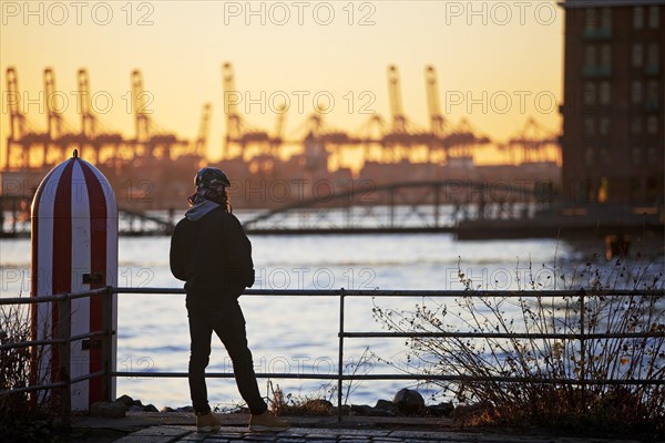 A person in front of loading cranes at the Norderelbe in Altona