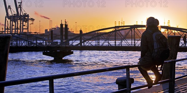 A woman sits on a railing at sunset on the Norderelbe in Altona