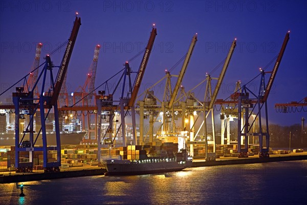 Loading cranes at the container terminal Burchardkai with a container ship in the evening