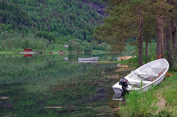 Small boat with outboard motor lying on the reflecting water of a green coloured body of water