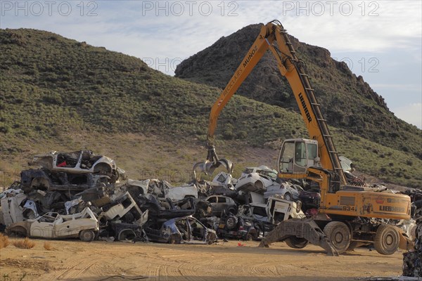 Crane piles scrap car on top of other cars