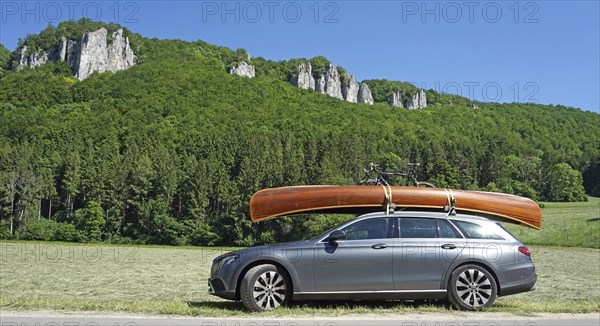 Mercedes with cedar wood canoe on roof in front of rocks in the Danube valley