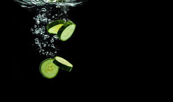 Sliced bio cucumber splashing water isolated on black background