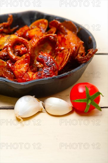 Fresh seafood stew prepared on an iron skillet ove white rustic wood table