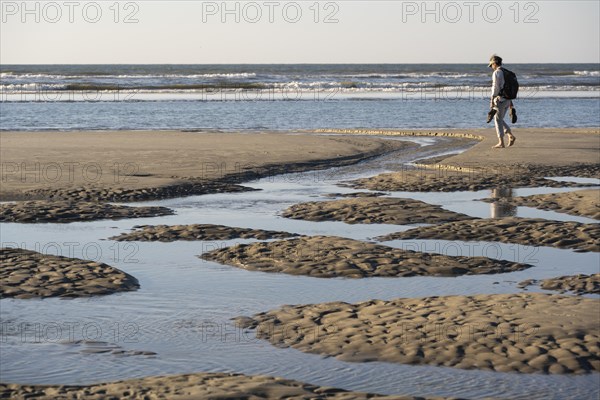 A walker on the beach at low tide with tide pools