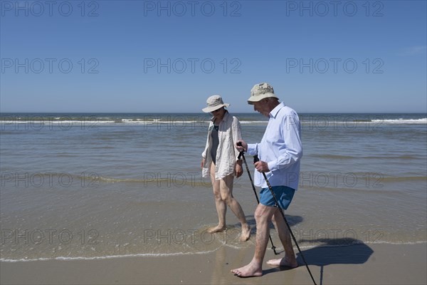 Elderly man accompanied by woman walking on the beach