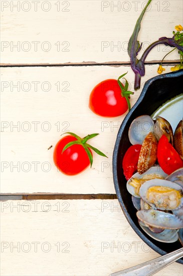 Fresh clams stewed on an iron skillet over wite rustic wood table