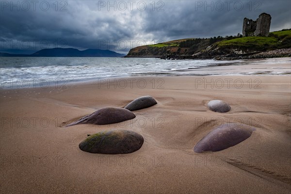 Sandy beach beach with stones and Minard Castle in the background