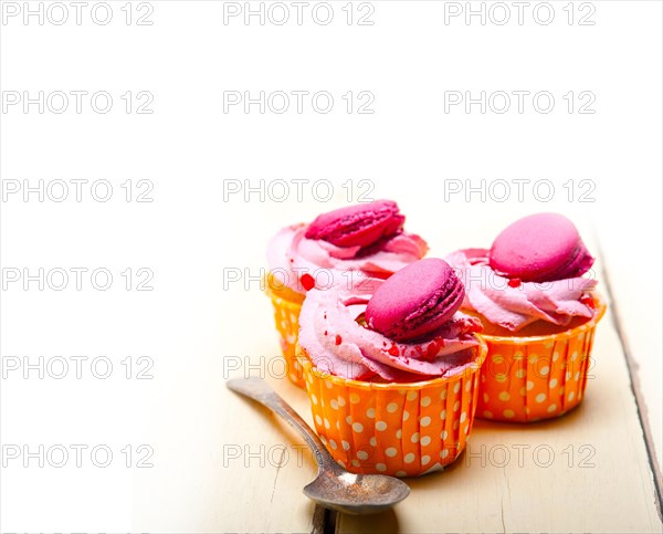 Fresh pink berry cream cupcake with macaroon on top over rustic wood table