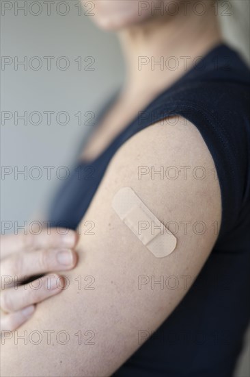 Arm of a woman with a plaster on her upper arm after vaccination