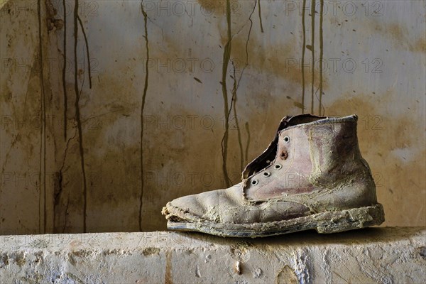 Ailing leather work boot stands on a wall