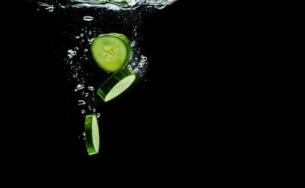 Sliced bio cucumber splashing water isolated on black background