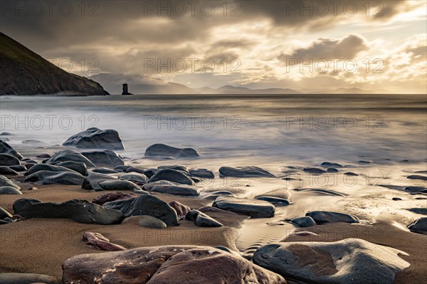 Sandy beach beach with stones on North Atlantic with rocky outcrop and cloudy sky