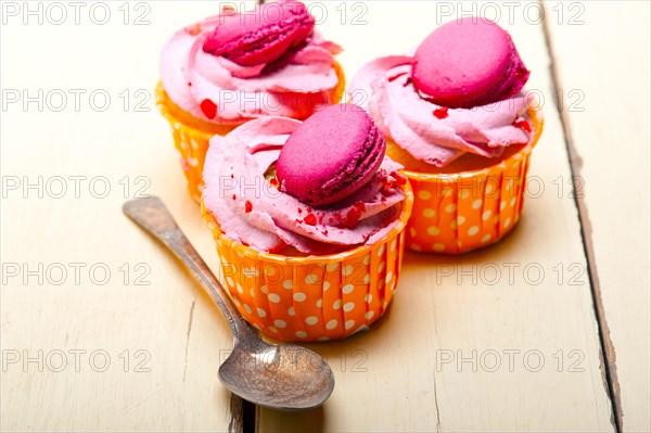 Fresh pink berry cream cupcake with macaroon on top over rustic wood table