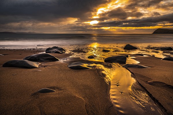 Sandy beach beach with stones on North Atlantic with rocky outcrop and cloudy sky at sunset