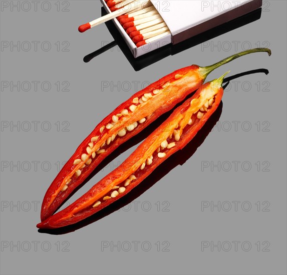 Fresh red chili peppers with matches over grey reflective surface